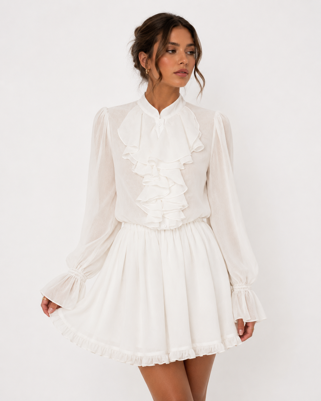 A woman modeling a white long-sleeve blouse and mini skirt set with ruffle details, photographed against a plain white studio background.